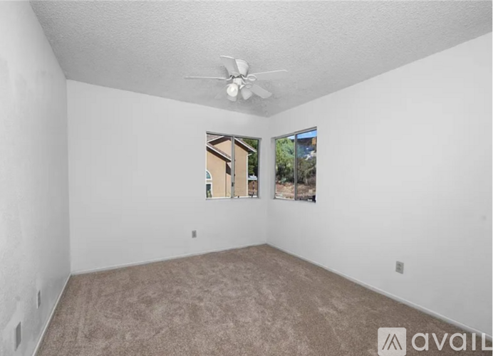 A room with a carpeted floor, a ceiling fan, and a window showing a view of a building.