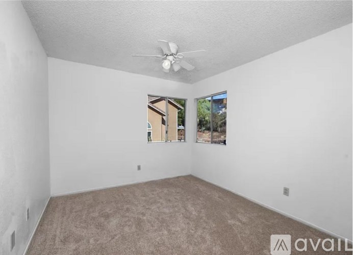A room with a carpeted floor, a ceiling fan, and a window showing a view of a building.