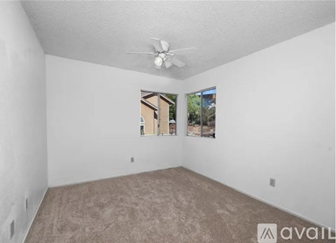 A room with a carpeted floor, a ceiling fan, and a window showing a view of a building.