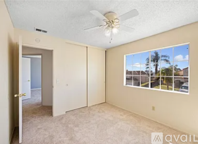 A room with a ceiling fan and a window showing a view of a residential area.