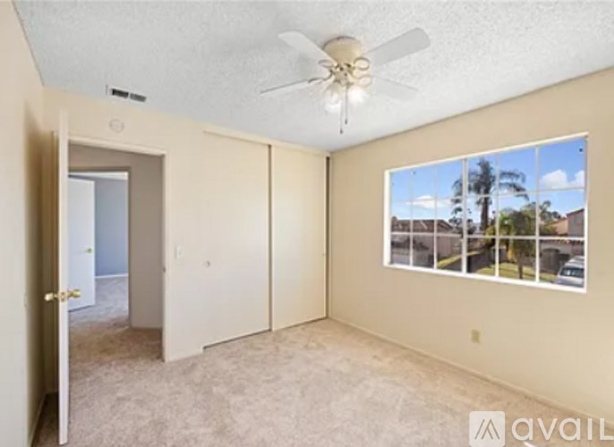A room with a ceiling fan and a window showing a view of a residential area.