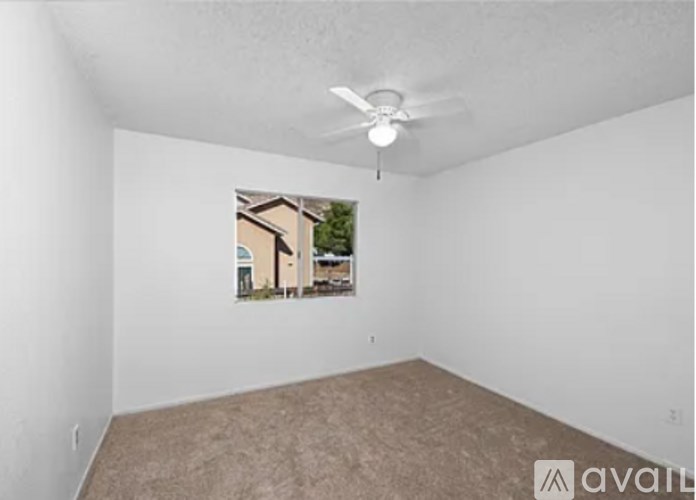 A room with a ceiling fan and a window showing a view of a house.