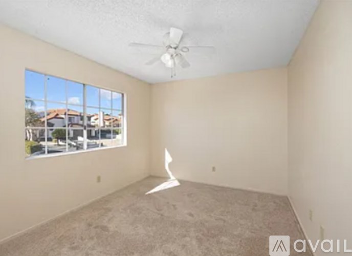 A room with a fan and a window showing a view of houses.