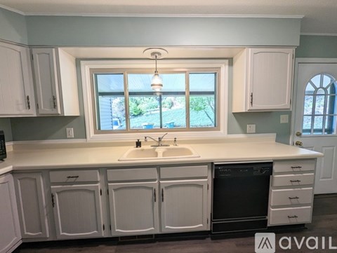 A kitchen with white cabinets and a window overlooking a backyard.