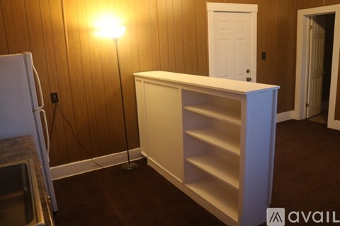 A white shelf unit sits in a room with a wooden wall and a white door.