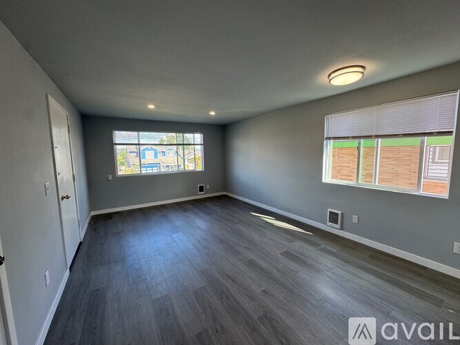 A spacious room with a large window and wooden flooring.