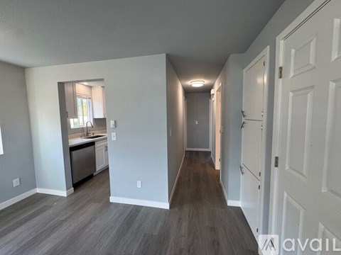 A long hallway with white doors and a kitchen area with a sink and a window.