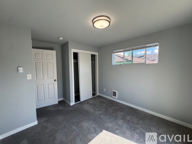 A room with a grey carpet and a window showing a view of a field.