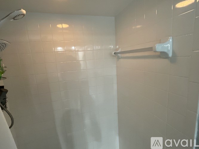 A white tiled shower with a white shower head and a white towel bar.