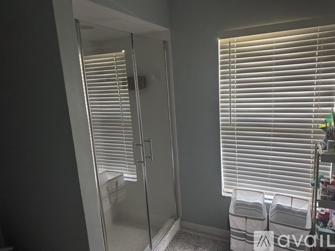 A bathroom with a glass shower door and a window with blinds.