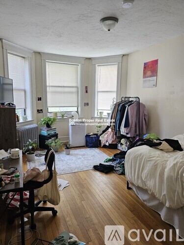 A room with a bed, desk, and clothing rack.