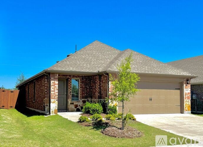A house with a brown brick exterior and a grey roof with a small tree in front.