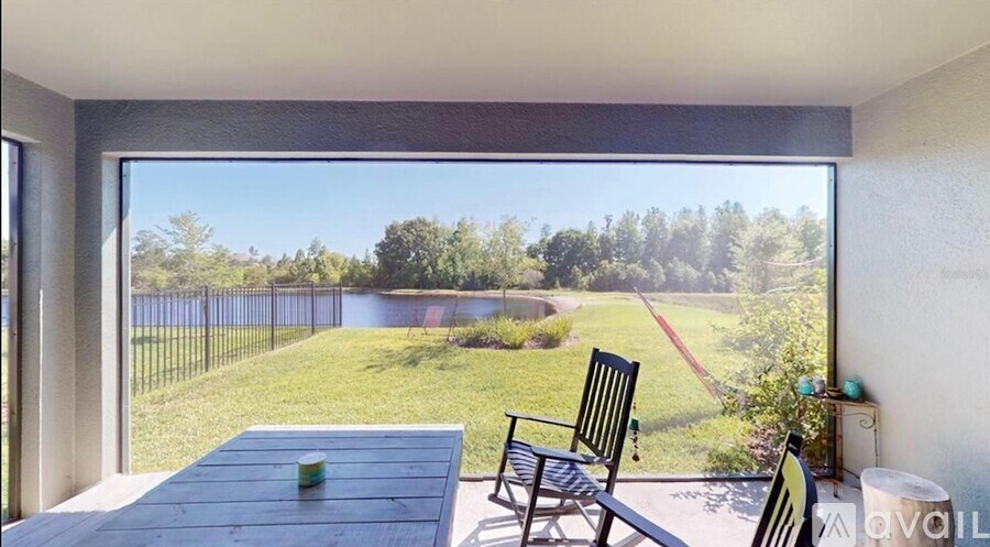 A patio with a table and chairs overlooks a green lawn and trees.