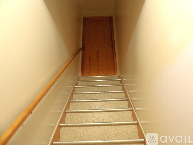 A staircase with a wooden handrail and beige carpeted steps leading to a wooden door.