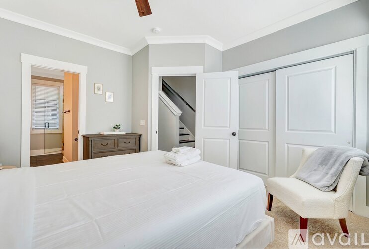 A bedroom with a white bed, chair, and ceiling fan.
