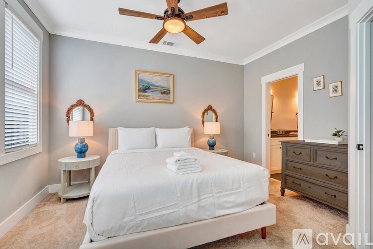 A bedroom with a bed, two lamps, a ceiling fan, and a painting on the wall.