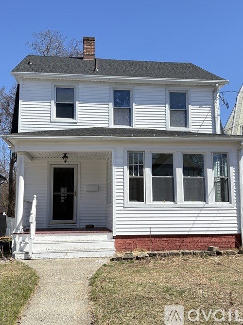 A white two-story house with a black roof and a brick foundation.