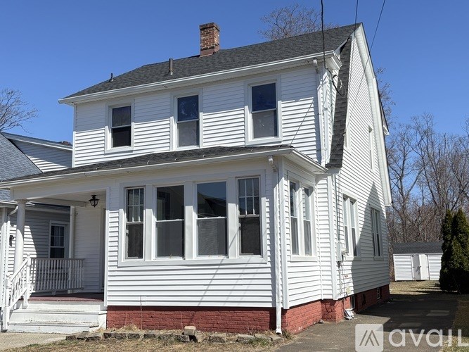 A two-story white house with a red brick foundation and a chimney.