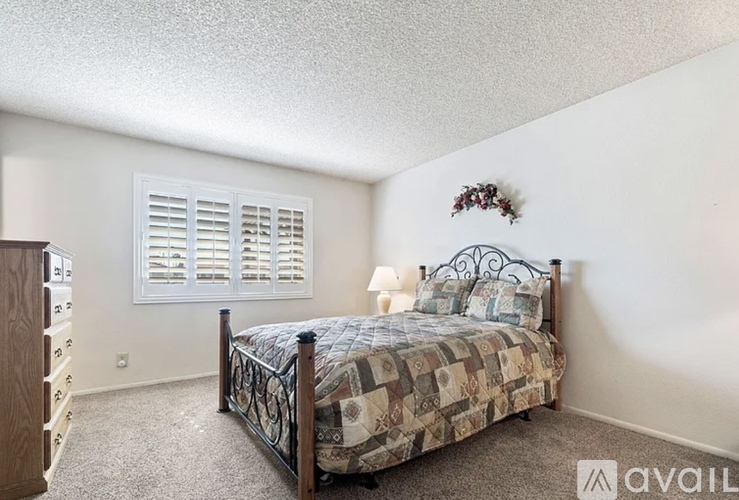 A bedroom with a bed, dresser, and window with shutters.