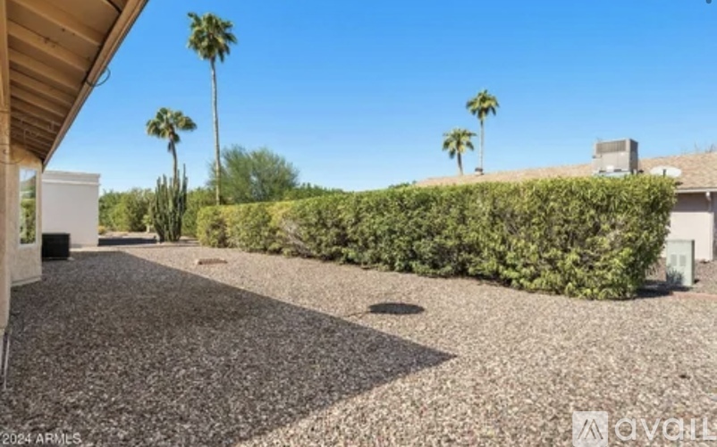 A gravel driveway leads to a house with a white garage door and a hedge on the side.