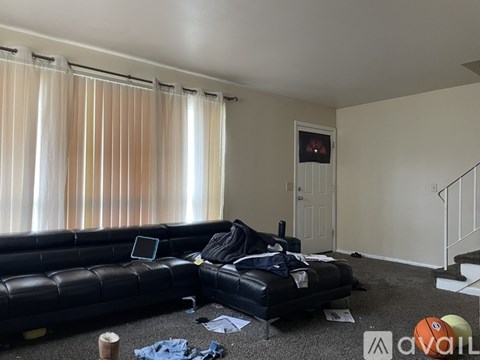 A living room with a black couch and a TV in the background.