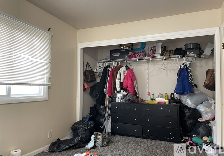 A messy bedroom with a black dresser and a window with blinds.