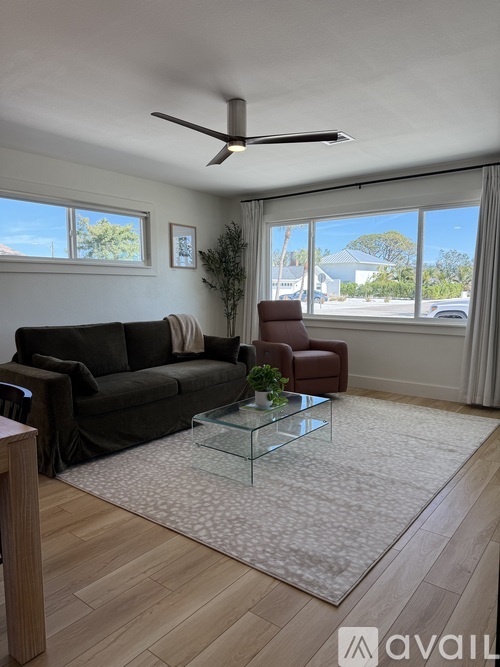 A living room with a black couch, a glass coffee table, and a ceiling fan.