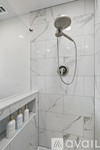 A shower head is mounted on a wall with marble tiles.