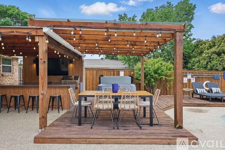 A wooden pergola with string lights is over a table set for dining outside.