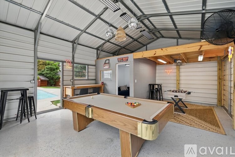A pool table is in the middle of a room with a refrigerator and a fan.