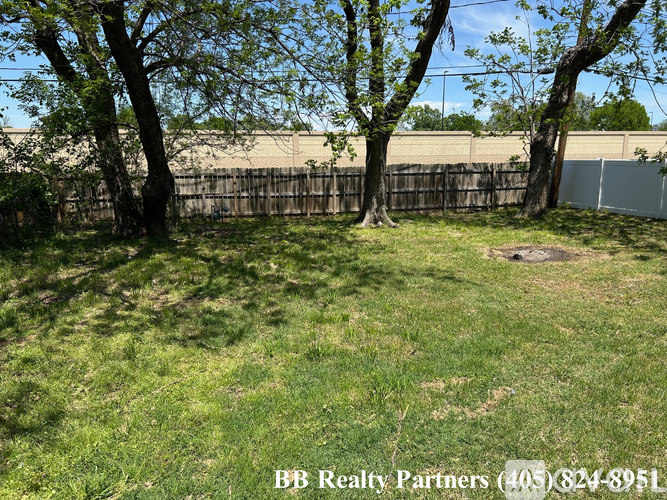 A grassy area with trees and a fence in the background.
