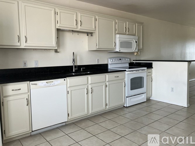 A kitchen with white cabinets and black countertops.