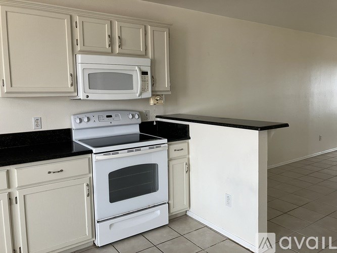 A kitchen with white cabinets and black countertops.