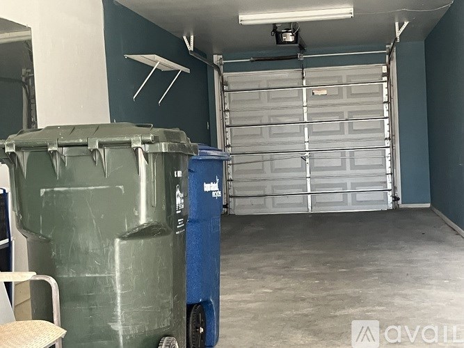 A room with a closed white garage door and a green dumpster.