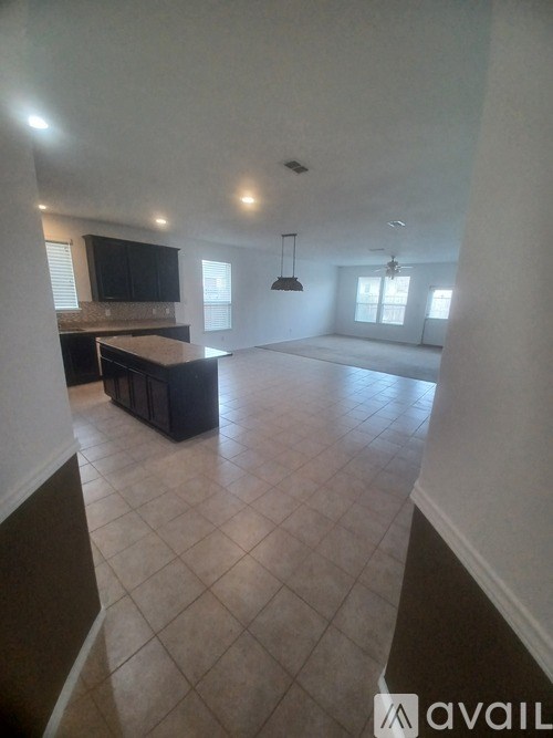 A spacious living room with a kitchen area in the background.