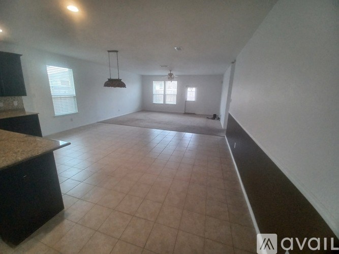 A spacious room with tiled flooring and a kitchen area with a counter and cabinets.