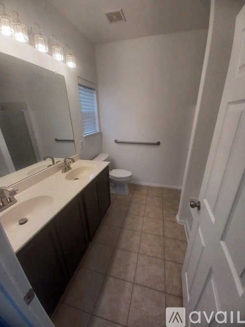 A bathroom with a toilet, sink, mirror, and lighting fixture.