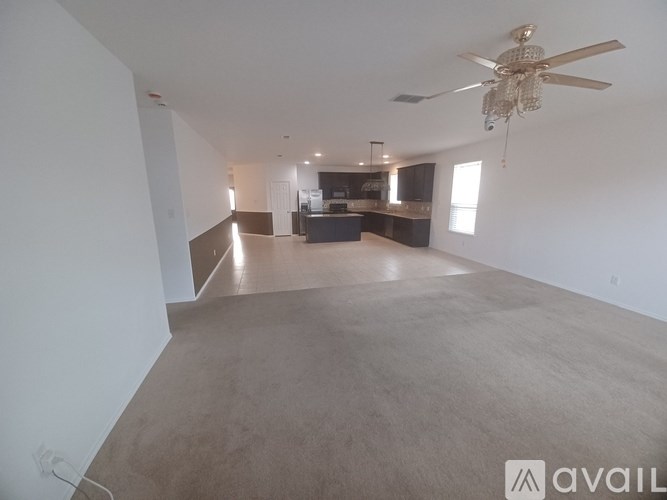 A spacious living room with a ceiling fan and a kitchen area in the background.