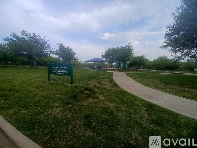 A green sign in a grassy area with a pathway leading to a pavilion.