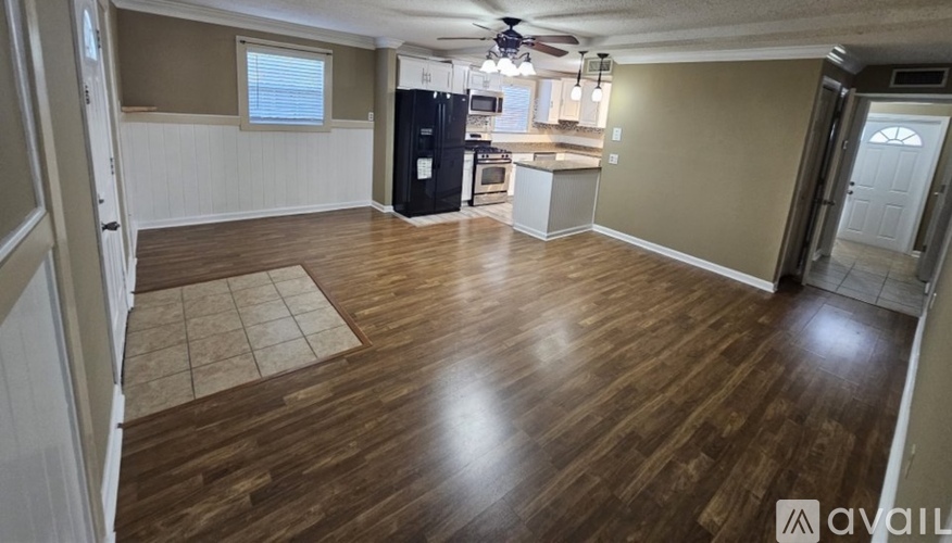 A spacious living room with wood flooring and a kitchen area in the background.