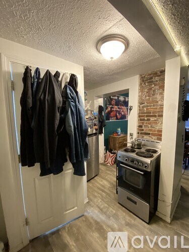 A kitchen with a stove and oven, a door with clothes hanging on it, and a brick wall.