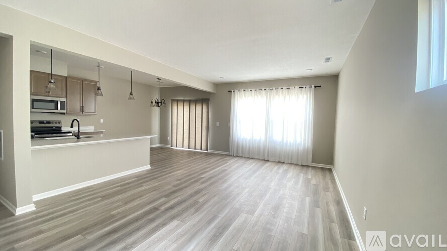 A spacious living room with wooden flooring and a kitchen area in the background.