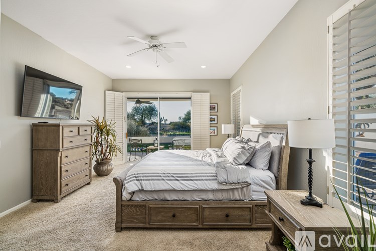 A bedroom with a large bed, a dresser, a ceiling fan, and a window with a view of the water.
