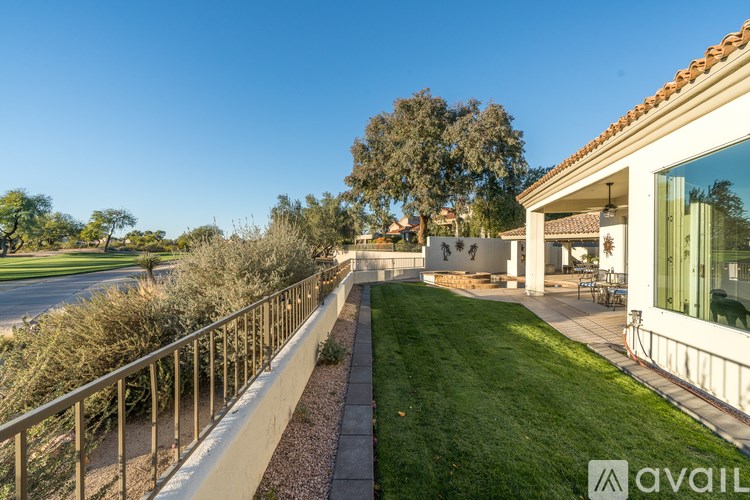 A balcony with a metal railing overlooks a green lawn and a building.