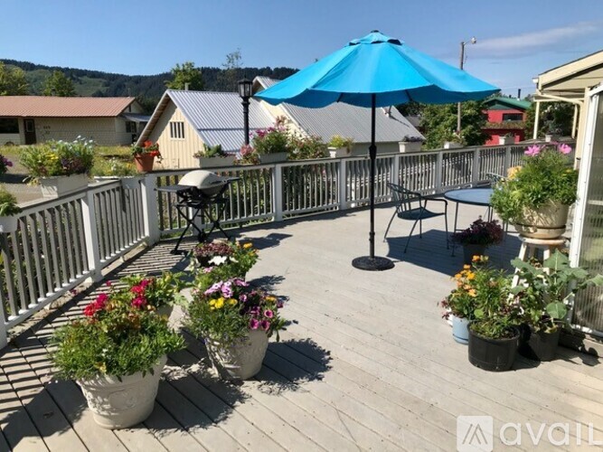 A blue umbrella is on a deck with potted plants.