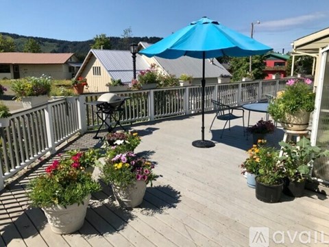 A blue umbrella is on a deck with potted plants.