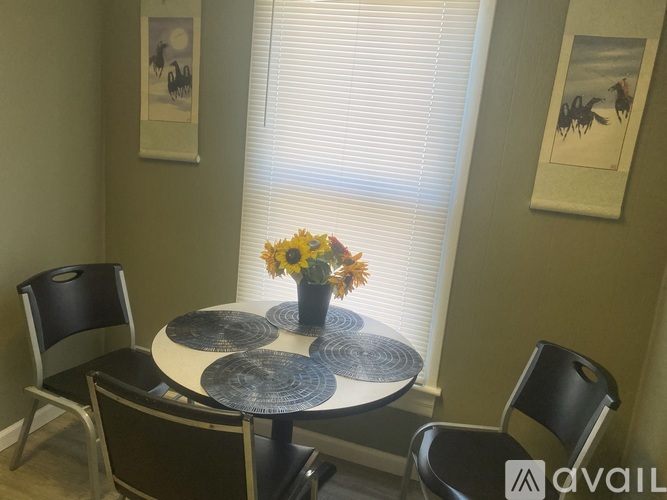 A dining table with chairs and a vase of flowers in front of a window.