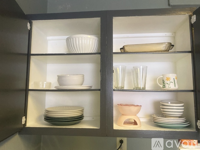 A kitchen cabinet with glass doors is open, revealing neatly arranged plates, bowls, and glasses.