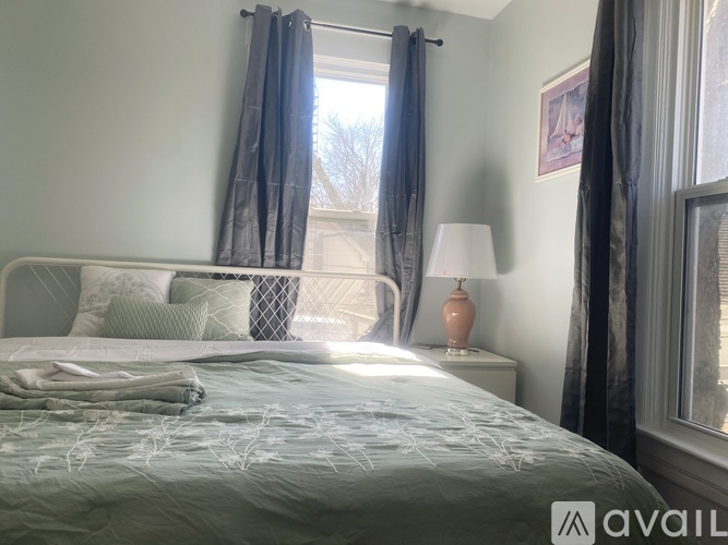 A bedroom with a bed, nightstand, and window with curtains.