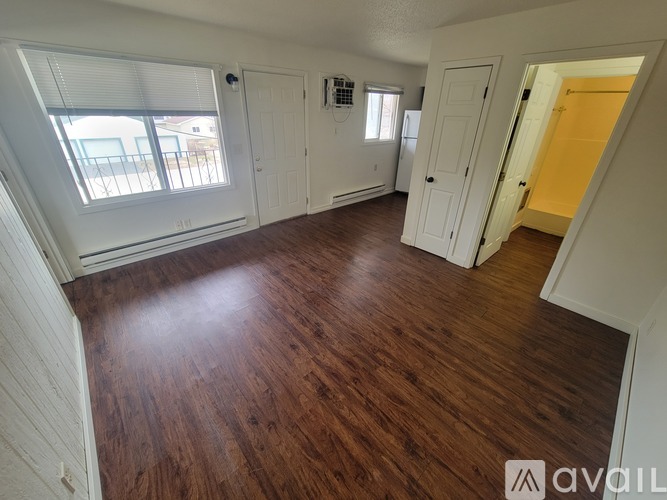 A room with wooden floors and white walls, with a window on the left side.